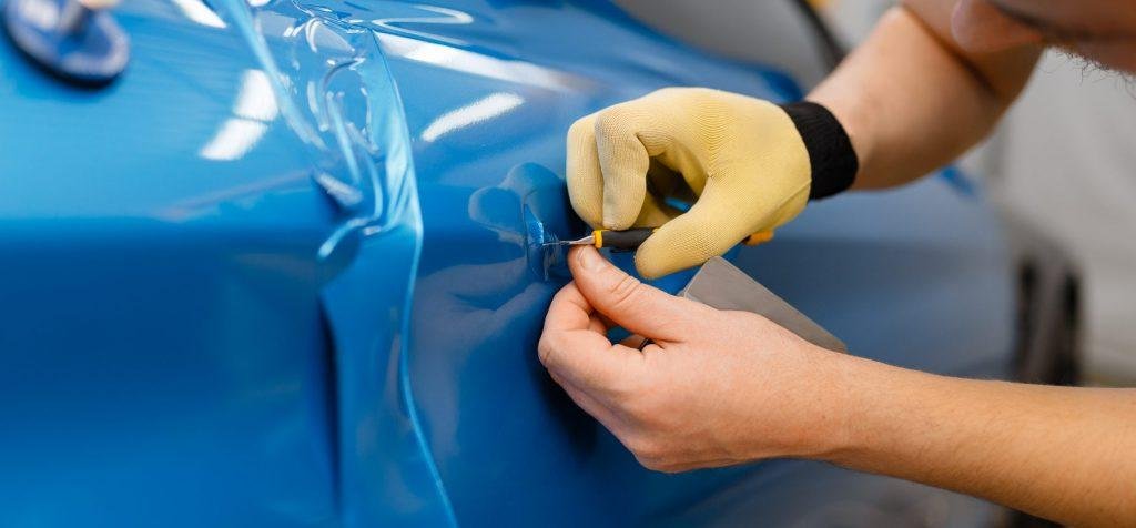 Car wrapper installs protective vinyl foil or film on vehicle door. Worker makes auto detailing. Automobile paint protection, professional tuning